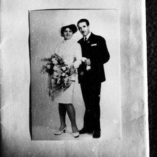 Couple in formal wear poses with flowers, likely a wedding.