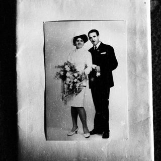 Couple in formal wear poses with flowers, likely a wedding.