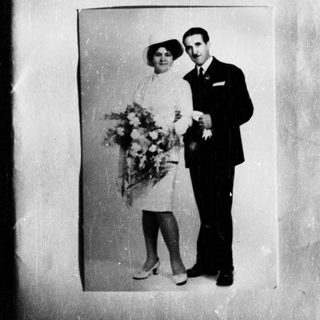 Couple in formal wear poses with flowers, likely a wedding.