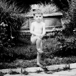 Here's a brief summary of the image: Barefoot boy sits in a garden, looking at the camera.
