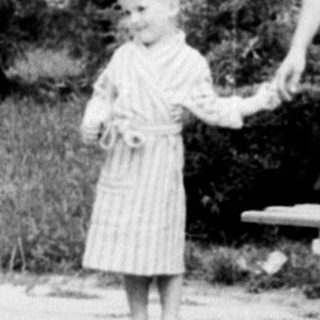 Woman and child walk along a path, building in background.