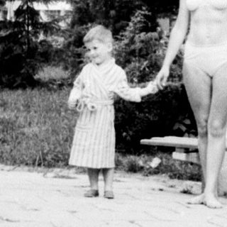 Woman and child walk along a path, building in background.