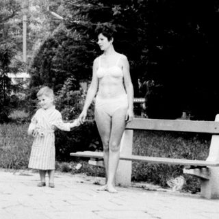 Woman and child walk along a path, building in background.