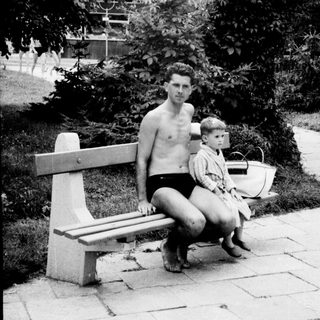 Man and child sit on a bench in a garden.