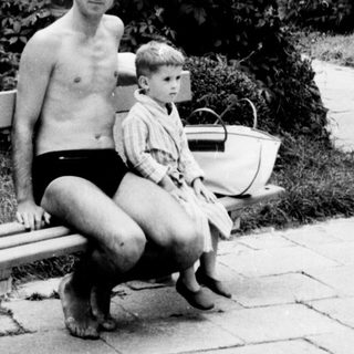 Man and child sit on a bench in a garden.