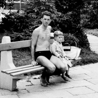 Man and child sit on a bench in a garden.