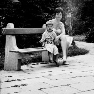 Here's a brief summary of the image: Woman and child sit on a bench in a garden.