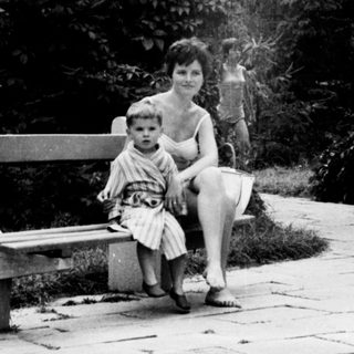 Here's a brief summary of the image: Woman and child sit on a bench in a garden.