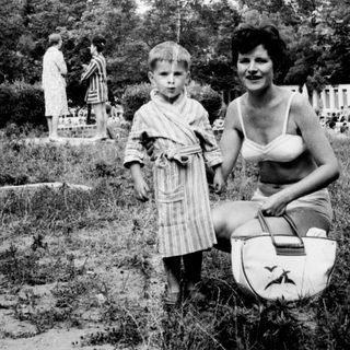 A child and woman outdoors, near a statue and foliage.