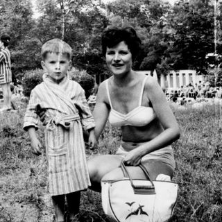 A child and woman outdoors, near a statue and foliage.