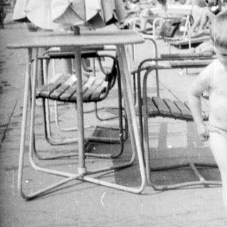 Boy runs near pool with sunbathers in the background.