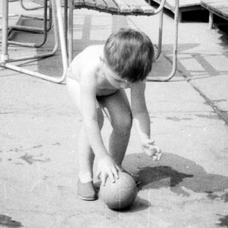 Here's a brief summary of the image: Child playing with a ball near a pool area.