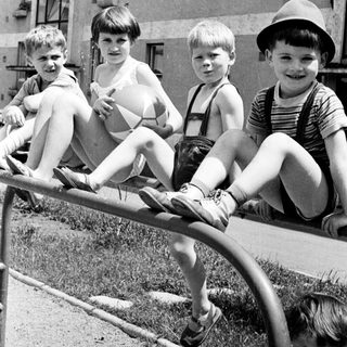 Four boys perch on a railing in a vintage photograph.