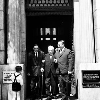 Here's a brief summary of the image: Three men exit a building; a boy watches nearby.