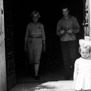 Two young children stand on steps; adults walk inside.