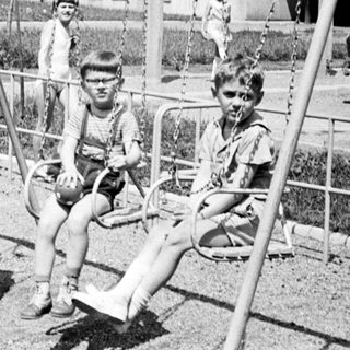 Black and white photo of children playing on swings.