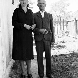 Older couple stands near a building in a rural setting.