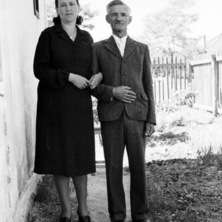 Older couple stands near a building in a rural setting.