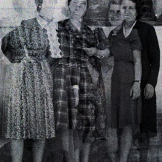 Four women stand outdoors, posing near a door and window.