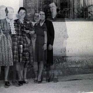 Four women stand outdoors, posing near a door and window.