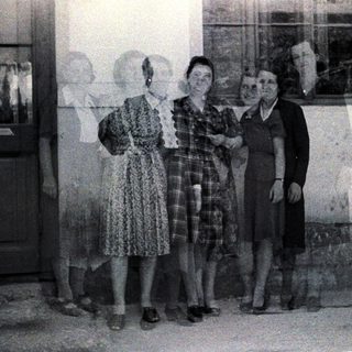 Four women stand outdoors, posing near a door and window.