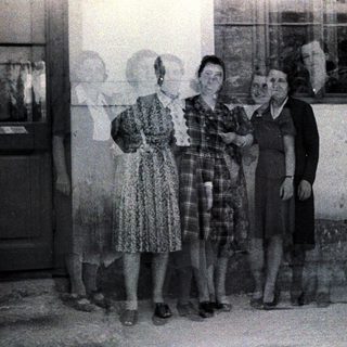 Four women stand outdoors, posing near a door and window.