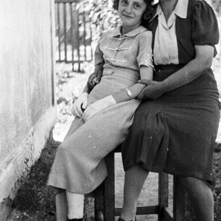 Two women seated outside a building in a monochrome photograph.
