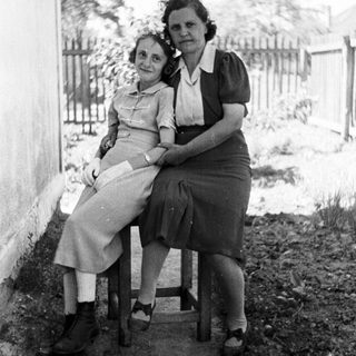 Two women seated outside a building in a monochrome photograph.