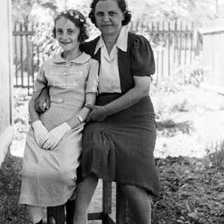 Two women seated outdoors, dressed in vintage clothing.