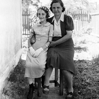 Two women seated outdoors, dressed in vintage clothing.