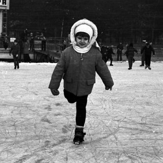 A child skates on an outdoor rink with onlookers.