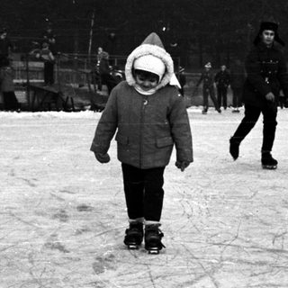 People ice skating outdoors with a building in the background.