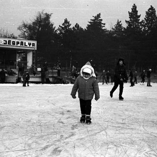 People ice skating outdoors with a building in the background.