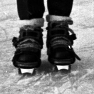 Child in skates stands on an outdoor ice rink.