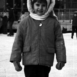 Child in skates stands on an outdoor ice rink.