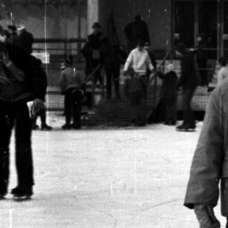 Child in skates stands on an outdoor ice rink.