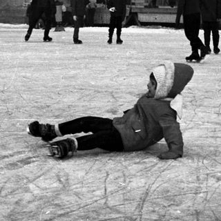 Child falls on ice rink with onlookers present.