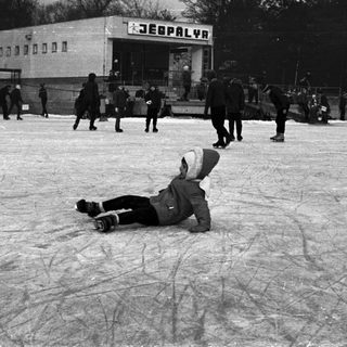 Child falls on ice rink with onlookers present.