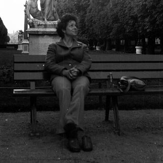 Here's a brief summary of the image: Person sits on a bench near a statue in a garden.