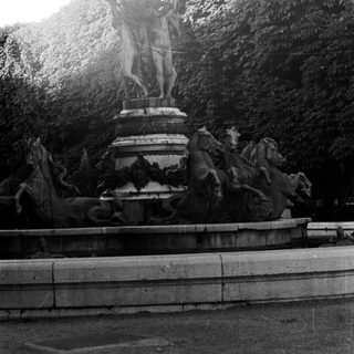 Monumental fountain depicts a man holding a globe, surrounded by horses.
