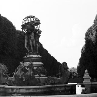 Monumental fountain with statues and a globe in a garden.