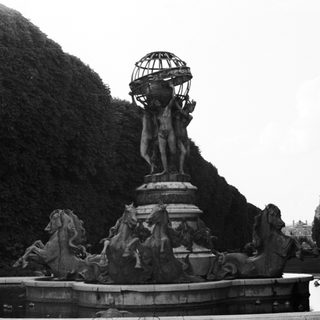 Monumental fountain with statues and a globe in a garden.