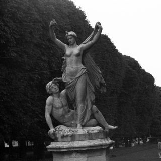 Classical sculpture stands in a formal, symmetrical garden landscape.