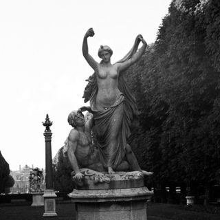 Classical statue of a woman standing over a man on pedestal.