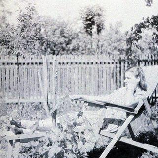 Woman relaxing in a chair outdoors, near a fence.