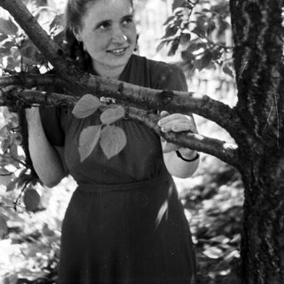 Woman smiles while holding a tree branch in a garden.
