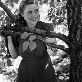 Woman smiles while holding a tree branch in a garden.