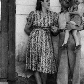 Man holding a baby, woman standing nearby outdoors.