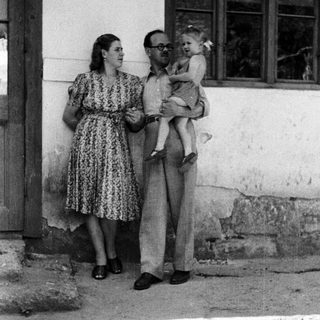 Man holding a baby, woman standing nearby outdoors.