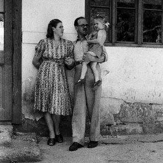 Man holding a baby, woman standing nearby outdoors.